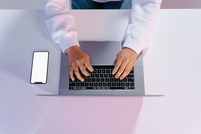 Hands typing on a laptop beside a phone